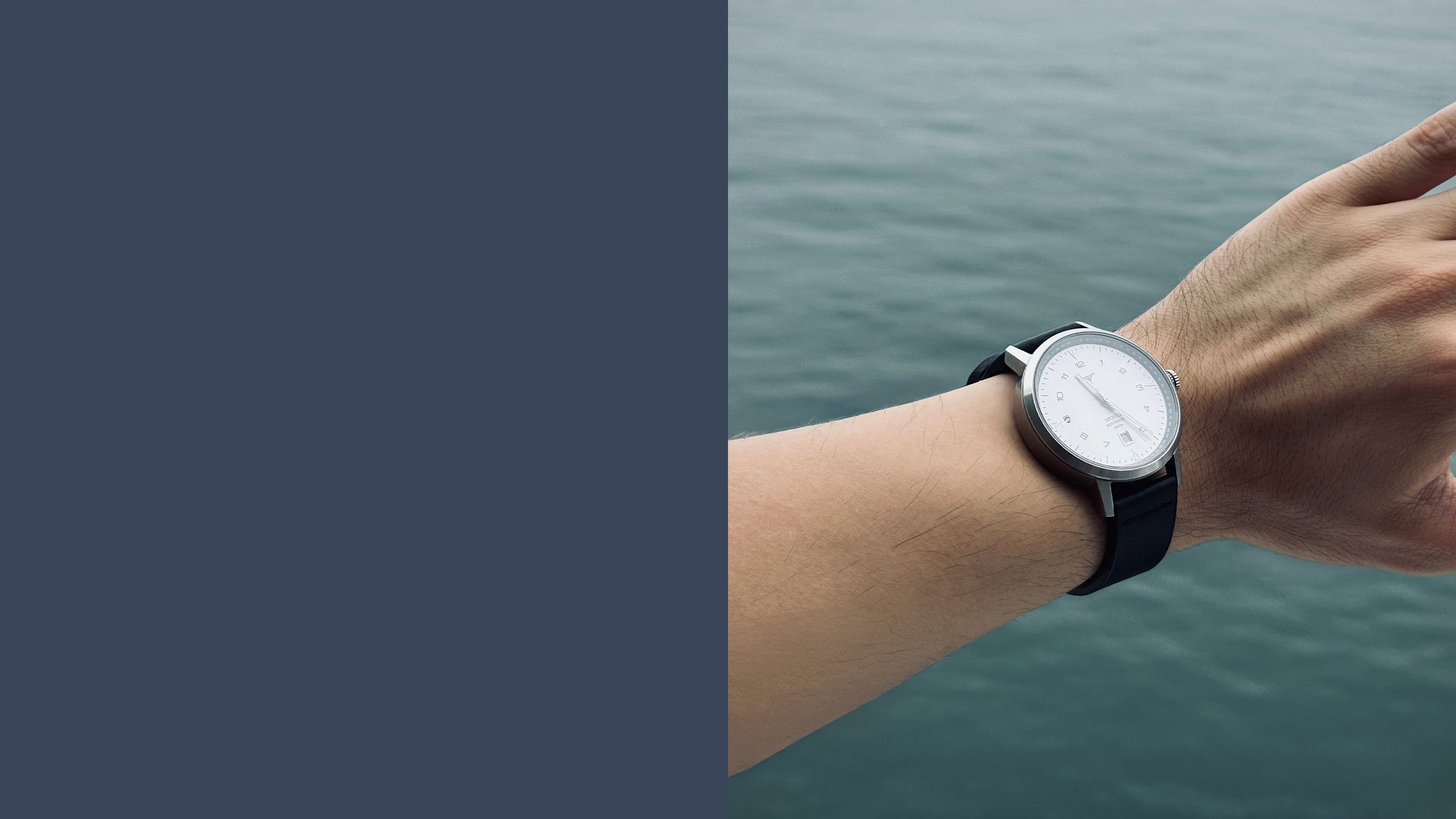 A minimalist analog wristwatch with a silver-toned case, white dial, and black strap worn on a person's wrist, with a blurred body of water in the background | White dial automatic watches V-Apostle with Black Horween Leather Straps | Vstelle Watch
